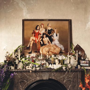 Retrato artístico de cinco mujeres en un marco grande sobre una chimenea decorada.