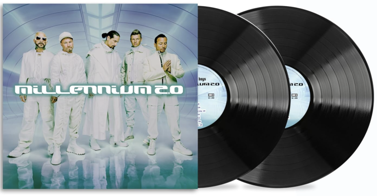 Grupo musical posando con álbum doble de vinilo en un fondo azul claro.